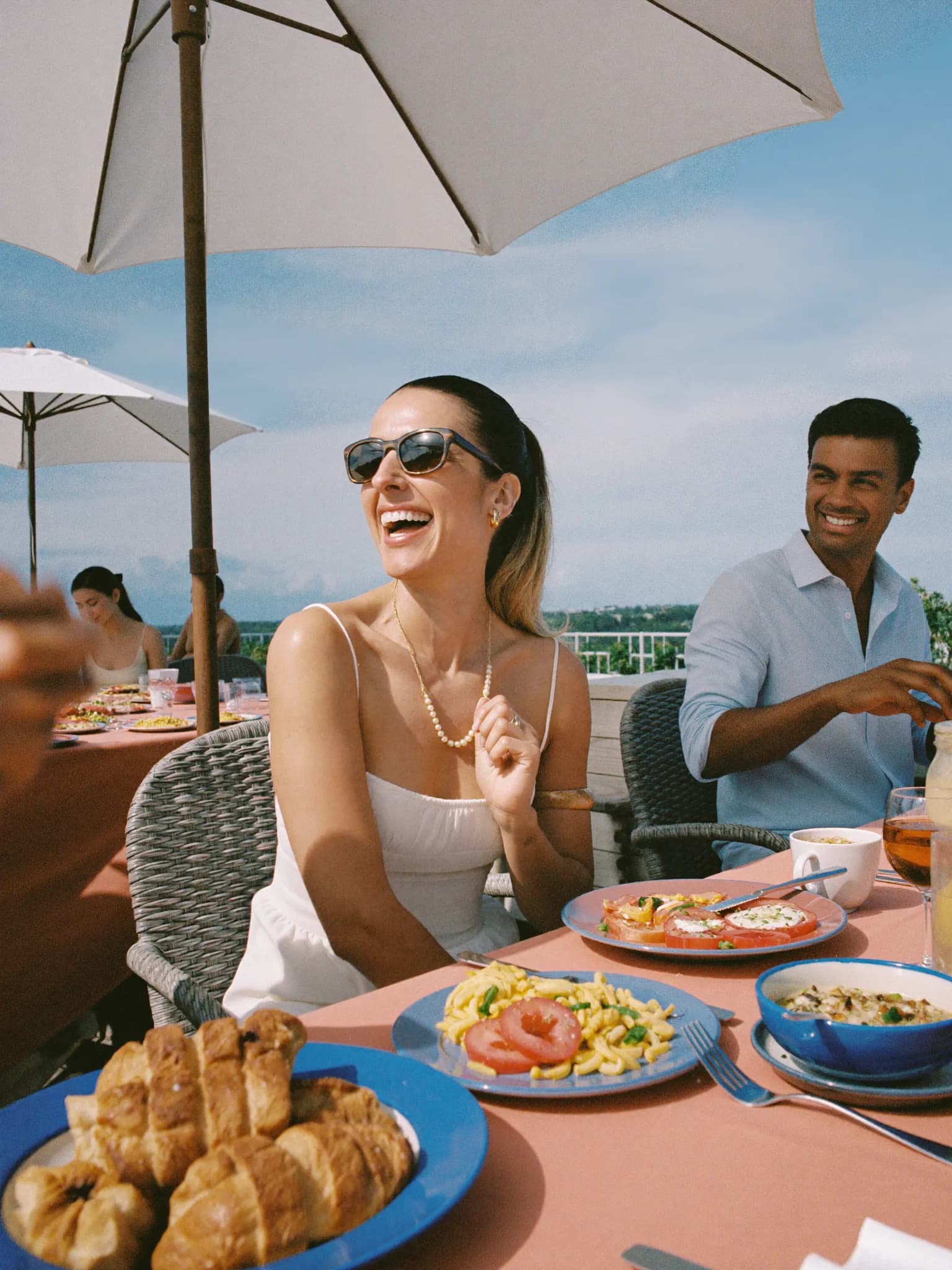 A woman in her late 40s laughing with friends at an outdoor brunch