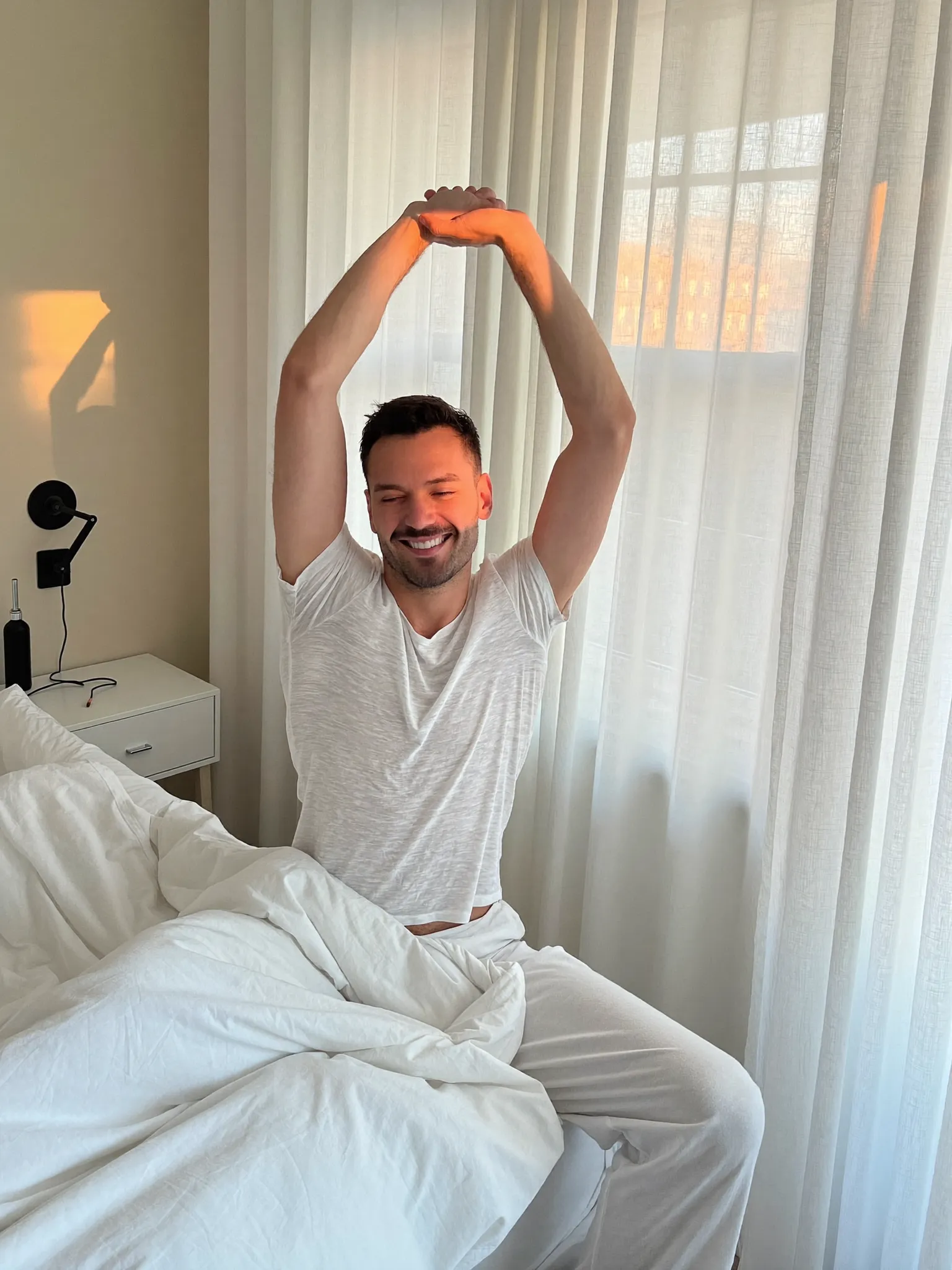 A man in his late 40s waking up refreshed in a bright, airy bedroom